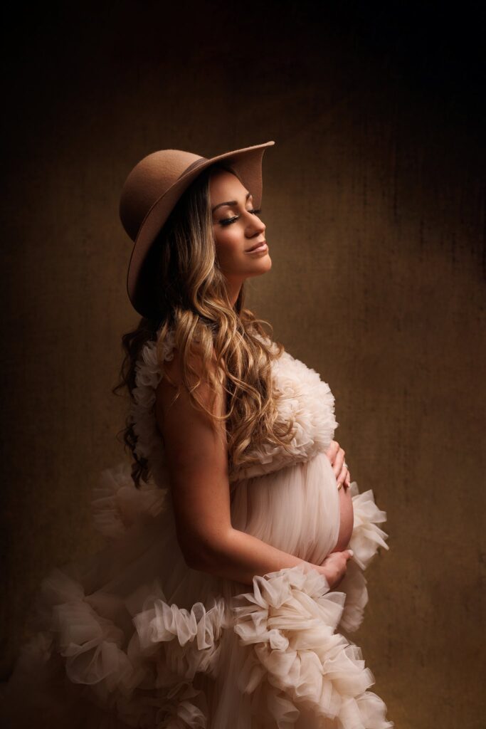 Beautiful mother to be in a cream fluffy maternity gown and brown trendy hat